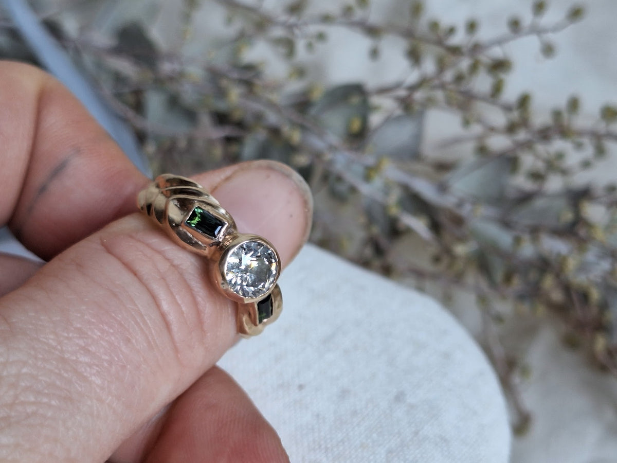 diamond centre set stone with baguette green tourmaline accent side stones in gold band with wheat detail on band side